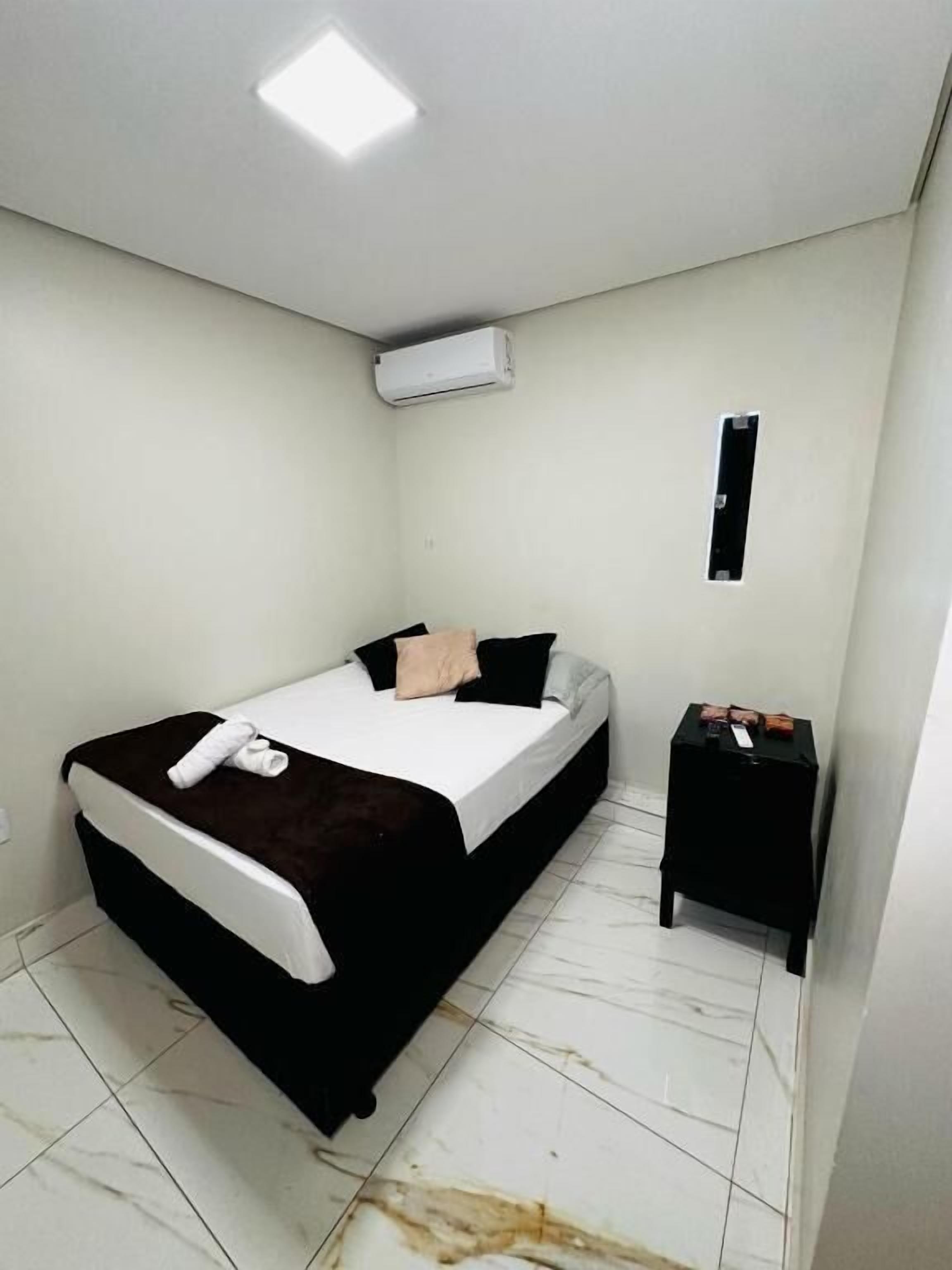 Ein kleines, sauberes Zimmer mit einem Bett, einem Nachttisch und einer Wand-Klimaanlage.