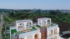 Un bâtiment moderne composé de deux structures blanches, dotées de fenêtres en arc de cercle et d’une terrasse sur le toit aménagée avec des sièges.