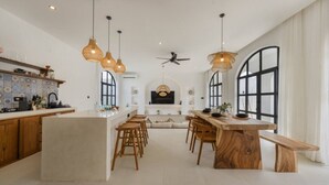 Une cuisine spacieuse dotée d’un îlot central, de tabourets de bar en bois, de luminaires suspendus et de grandes fenêtres.