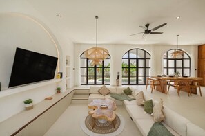 A spacious living room with a large TV, a dining area with a wooden table and chairs, and a cozy seating area with a sofa and a coffee table.