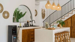 Une cuisine moderne dotée d’un îlot central, de meubles en bois, d’un distributeur d’eau intégré et d’un escalier avec une rampe.