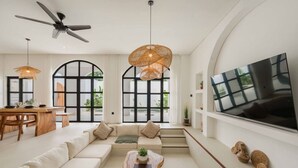 Un salon moderne doté d’un grand téléviseur, d’un ventilateur de plafond et d’un coin repas avec une table et des chaises en bois.