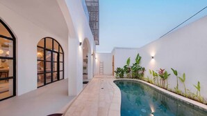 Une piscine intérieure moderne, dotée d’un design incurvé, entourée de murs blancs et agrémentée de quelques plantes.