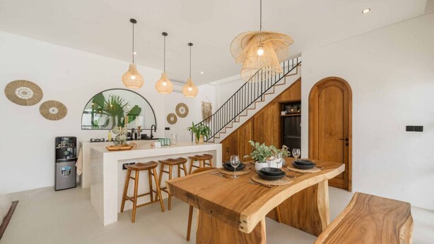Une cuisine moderne dotée d’un îlot central, de tabourets de bar en bois et de luminaires suspendus.