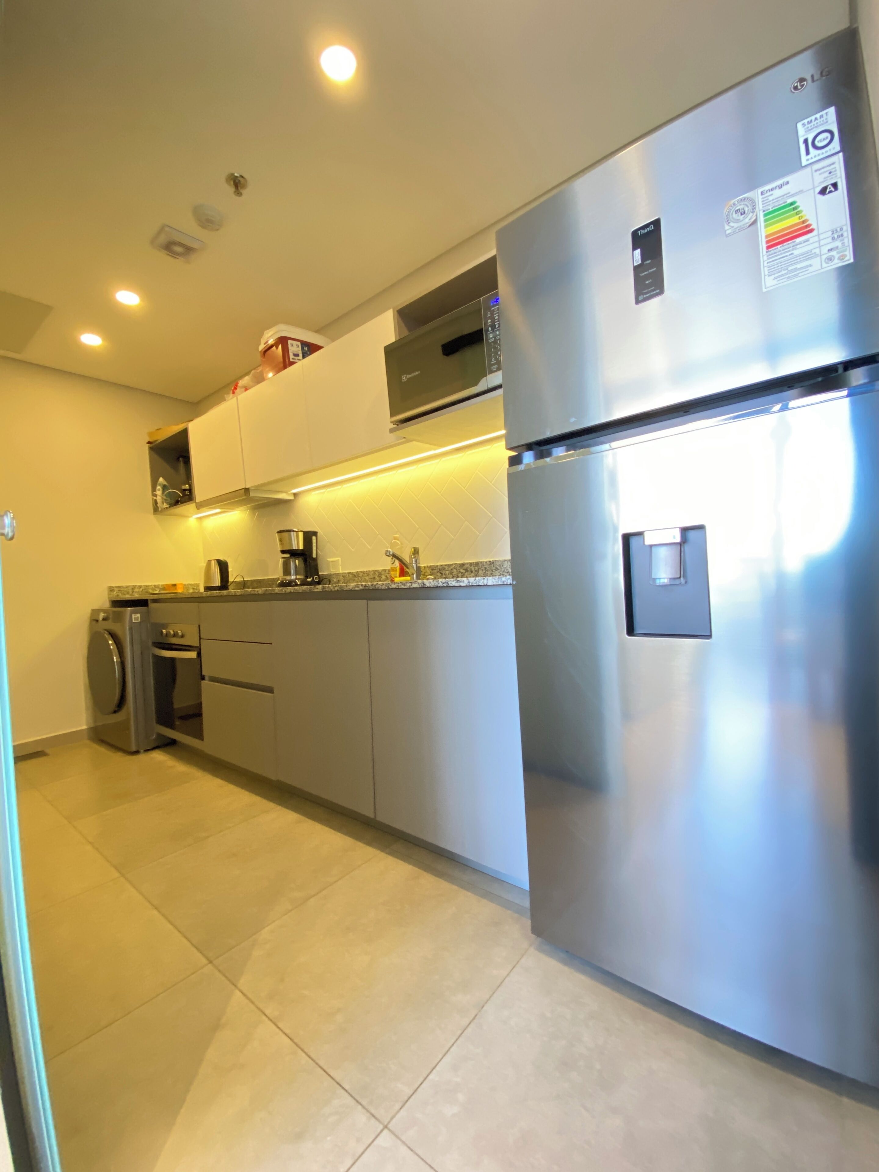 Una cocina moderna con electrodomésticos de acero inoxidable, incluyendo un refrigerador y una lavadora, además de un microondas sobre el horno.