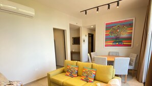 Una sala de estar moderna con un sofá amarillo, una mesa de comedor y un cuadro de colores en la pared.