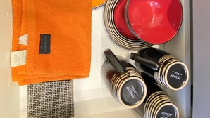 Un cajón con una pila de toallas naranjas, un paño estampado, una bandeja de madera con un mantel a cuadros, un cuenco rojo, un plato rojo y varias botellas a rayas negras y blancas.