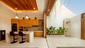 A modern kitchen with wooden cabinets, a central island, and hanging plants. - Modern 1BR Oasis - Sunken Lounge & Near Canggu (Mengwi)