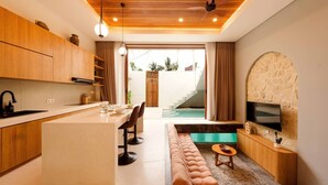 A modern kitchen with wooden cabinets, a central island, and a dining area with a sofa and chairs. - Modern 1BR Oasis - Sunken Lounge & Near Canggu (Mengwi)
