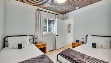 A hotel room with two beds, a window with blinds, a door, and a ceiling with a wooden panel design.