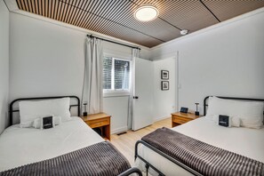 A hotel room with two beds, a window with blinds, a door, and a ceiling with a wooden panel design.
