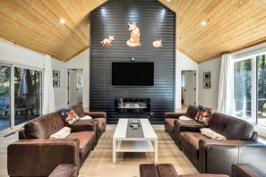 A modern living room with leather sofas, a central coffee table, a fireplace, and a large TV screen.