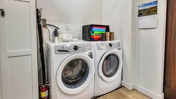 A laundry area with two white front-loading washing machines, a fire extinguisher, and a calendar on the wall.