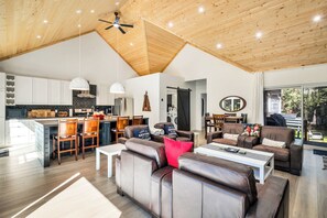 A spacious living area with a high ceiling, a kitchen with modern appliances, and a dining area with wooden furniture.