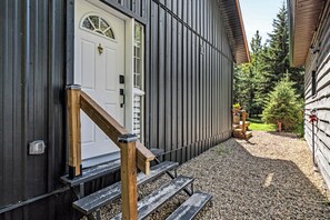 A wooden staircase leading to a white door with a window, a metal fence, and a gravel path.