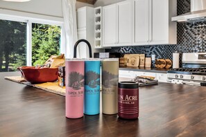 A kitchen with white cabinets, a black backsplash, and a wooden countertop. There are three beverage containers labeled 'Aspen Acre' and a red mug.
