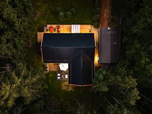 Vue aérienne d’une maison dotée d’une grande terrasse, d’un bâtiment annexe et entourée d’arbres denses.