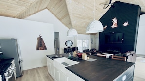 Eine moderne Küche mit Kochinsel, weißen Schränken und dunkler Arbeitsplatte. Die Decke ist aus Holz und eine Wand ist mit Fuchs-Motiven versehen.