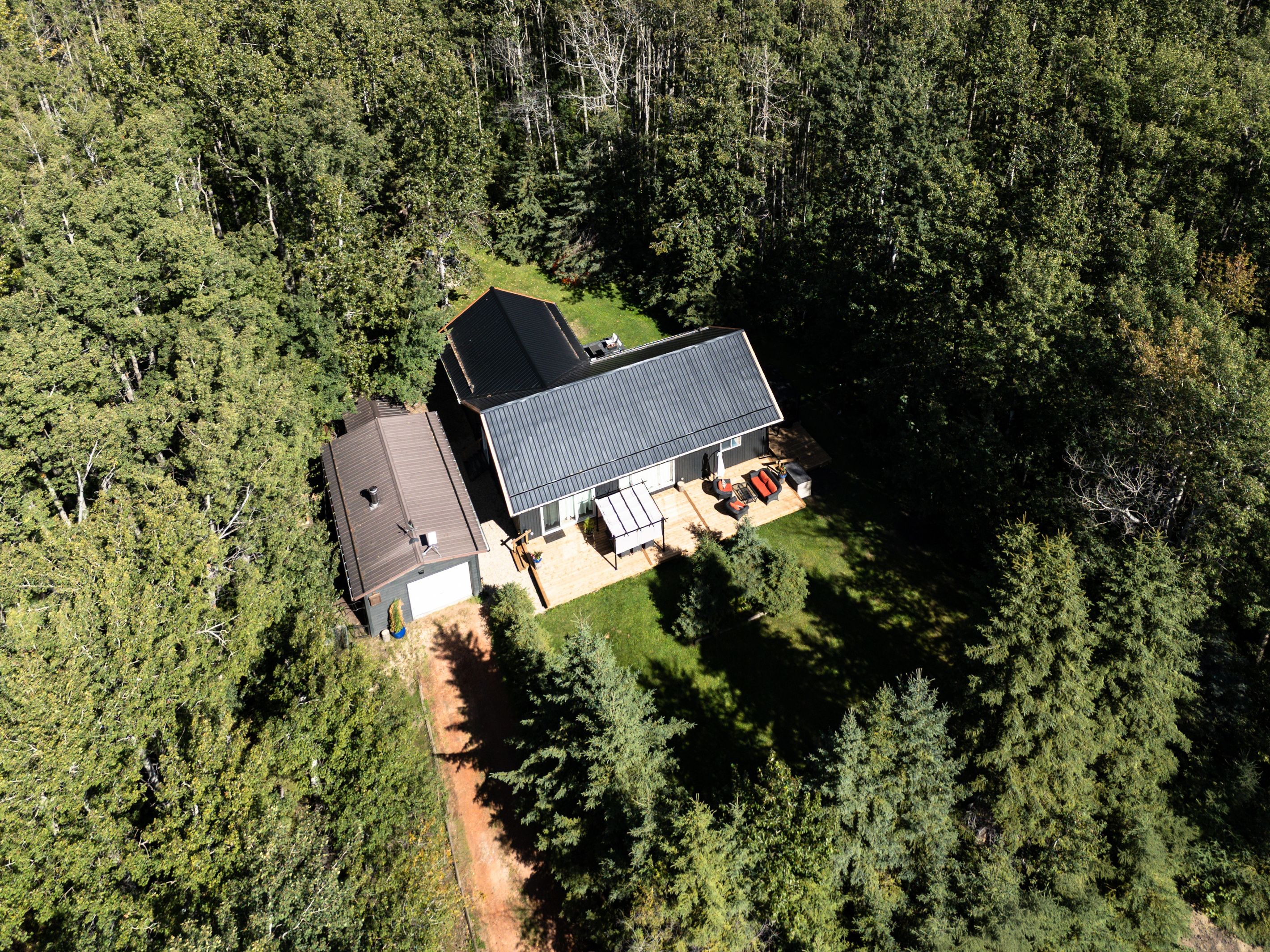 A two-story house with a large deck and a garage, surrounded by dense forest.