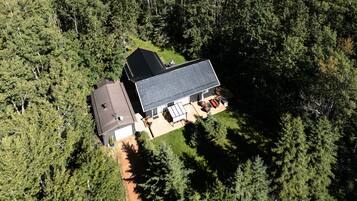 A two-story house with a large deck and a garage, surrounded by dense forest.