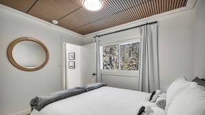 A bedroom with a bed, a round mirror, a window with curtains, and a door. - Aspen Acre @ Pigeon Lake Hot Tub Fire Pit StarLink (Poplar Bay)