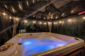 Un bain à remous doté d’un panneau de commande, entouré d’une structure recouverte de guirlandes lumineuses.