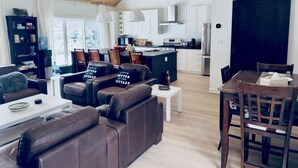 Ein modernes Wohnzimmer mit Ledersofas, einem Esstisch und einer Küche im Hintergrund.
