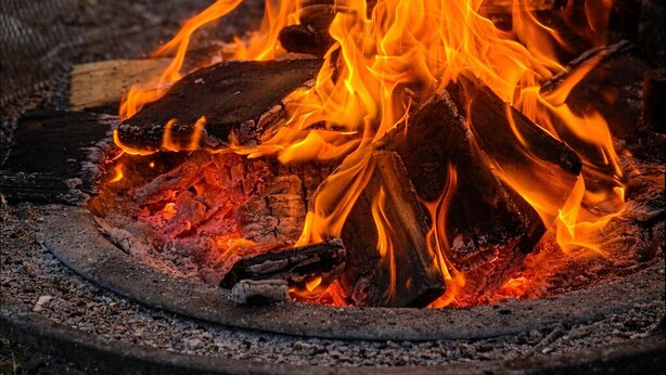 A campfire with logs and burning embers in a circular fire pit. - Aspen Acre @ Pigeon Lake Hot Tub Fire Pit StarLink (Poplar Bay)
