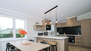 A modern kitchen with a central island, wooden cabinets, and a dining area with a table and chairs. - Poppy (Leominster)