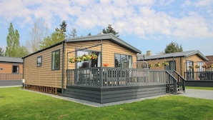 A single-story wooden mobile home with a balcony, a small porch, and a gravel driveway. - Poppy (Leominster)