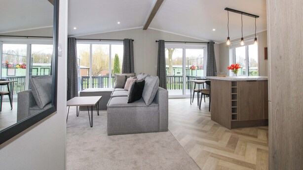A modern living room with a grey sofa, a small table, and a kitchen area with a bar counter. - Poppy (Leominster)