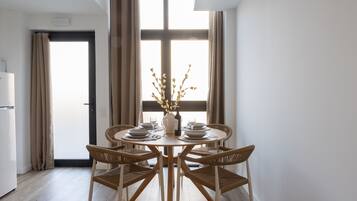Een eetruimte met een ronde tafel, vier rieten stoelen en een vaas met takken.
