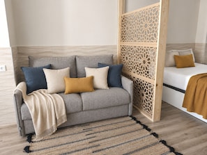A neutral-toned living room with a grey sofa, a patterned rug, and a wooden partition. - Valencia Urban Suite VI | 4 Guests | A/C & Wi-Fi | Near the City Center (Valencia)