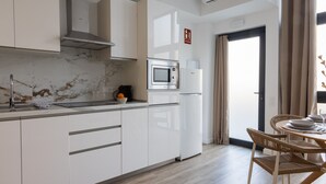 Una cocina moderna con armarios blancos, microondas integrado y refrigerador. Hay un comedor con una mesa y sillas.