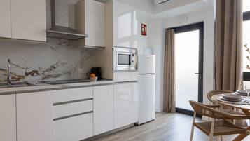 Een moderne keuken met witte kasten, een ingebouwde magnetron en een koelkast. Er is een eethoek met een tafel en stoelen.