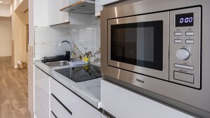 Una cocina moderna con un microondas de acero inoxidable, un reloj digital y un lavabo con escurreplatos.