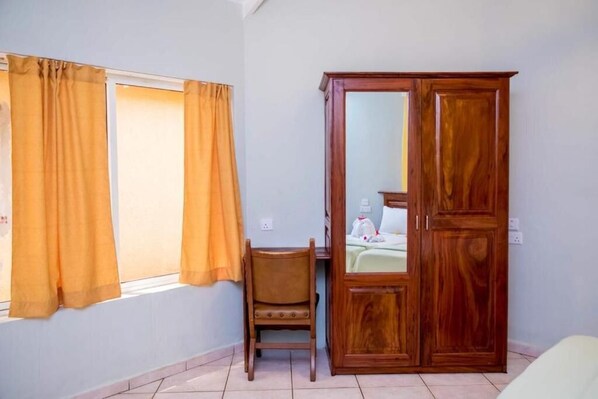A room with a wooden wardrobe, a chair, and a bed with a green bedspread. - TROPIC GARDEN HOTEL (Bakau)