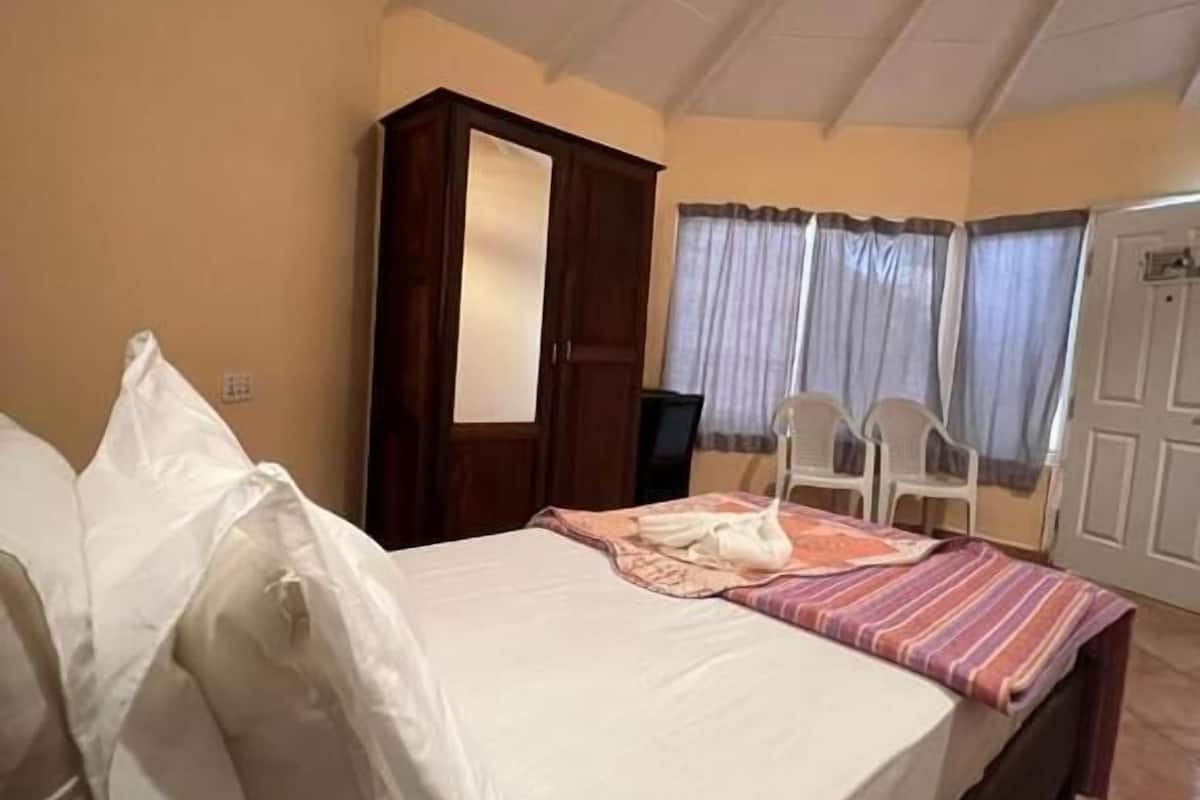 Un dormitorio con cama, armario, silla y ventana con cortinas.