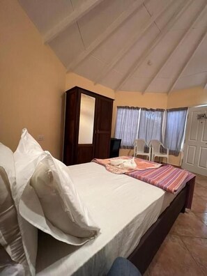 Ein Schlafzimmer mit Bett, Kleiderschrank, Stuhl und einem Fenster mit Vorhängen.