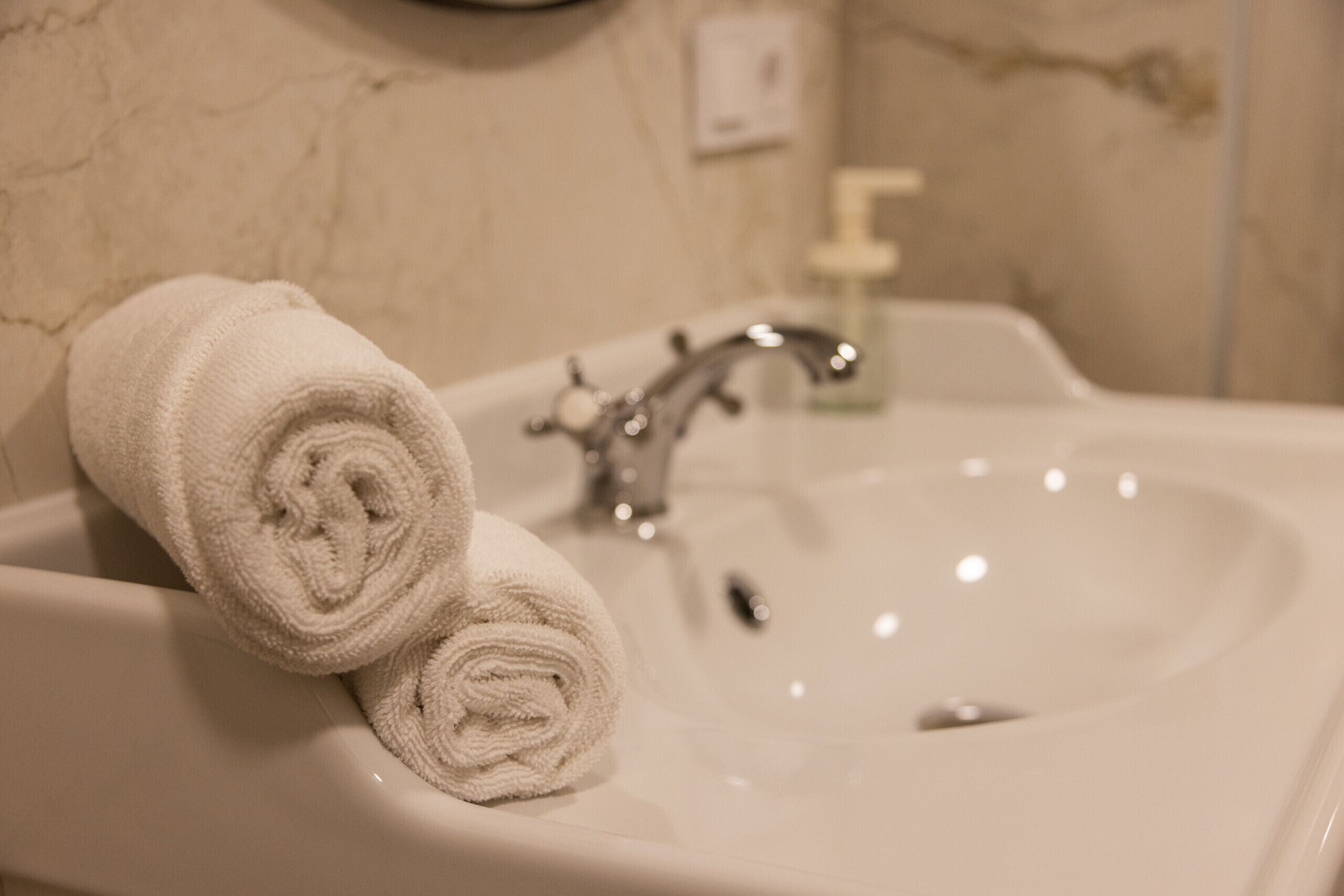 A bathroom sink with two rolled towels placed on it.