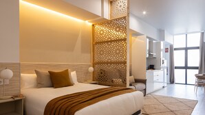 Een moderne hotelkamer met een groot bed, nachtkastjes, een decoratieve scheidingswand, een kitchenette en uitzicht op het buiten.