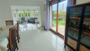 A spacious living area with a dining table, chairs, a sofa, and a glass cabinet. - Charming house in a quiet location, in the center of town, less than 800 m from the beach and all amenities (Cabourg)