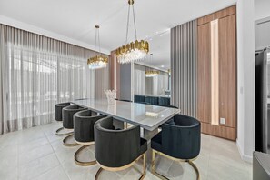 Uma área de refeições moderna com mesa de vidro, cadeiras pretas e um lustre.