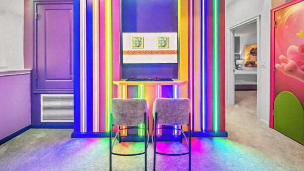 Un pasillo con un muro iluminado con neón, dos sillas y una pequeña mesa con una obra de arte.