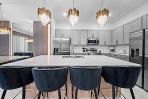 A modern kitchen with a large island, stainless steel appliances, and dark bar stools. - 10BR house with private pool in Paradiso Grande (Orlando)