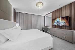 Ein modernes Hotelzimmer mit einem großen Bett, einem an einer Holzvertäfelung befestigten Fernseher und einem großen Spiegel über dem Schminktisch.