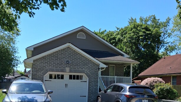 Une maison à deux étages avec un garage, deux voitures garées et une allée pavée en briques.