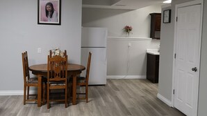 Une cuisine de taille réduite, équipée d’un réfrigérateur, d’une table à manger avec des chaises et d’une horloge murale.