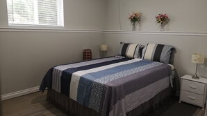 Une chambre à coucher comprenant un lit, des tables de chevet, une fenêtre et deux compositions florales fixées au mur.
