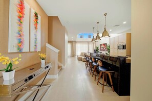 A modern kitchen with a central island, bar stools, pendant lighting, and a staircase leading to an upper level. - 3BR house near Disney with private pool (Kissimmee)
